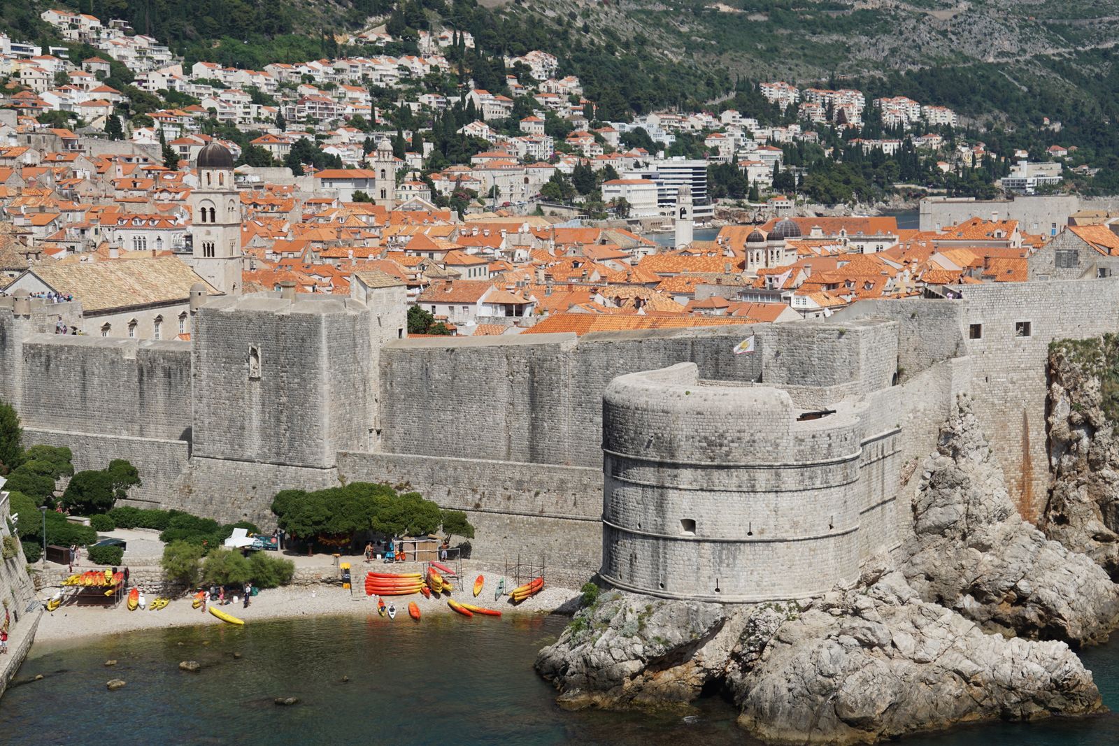 Dubrovnik city walls and a round bastion above a small cove with kayaks, and the Old Town rooftops behind