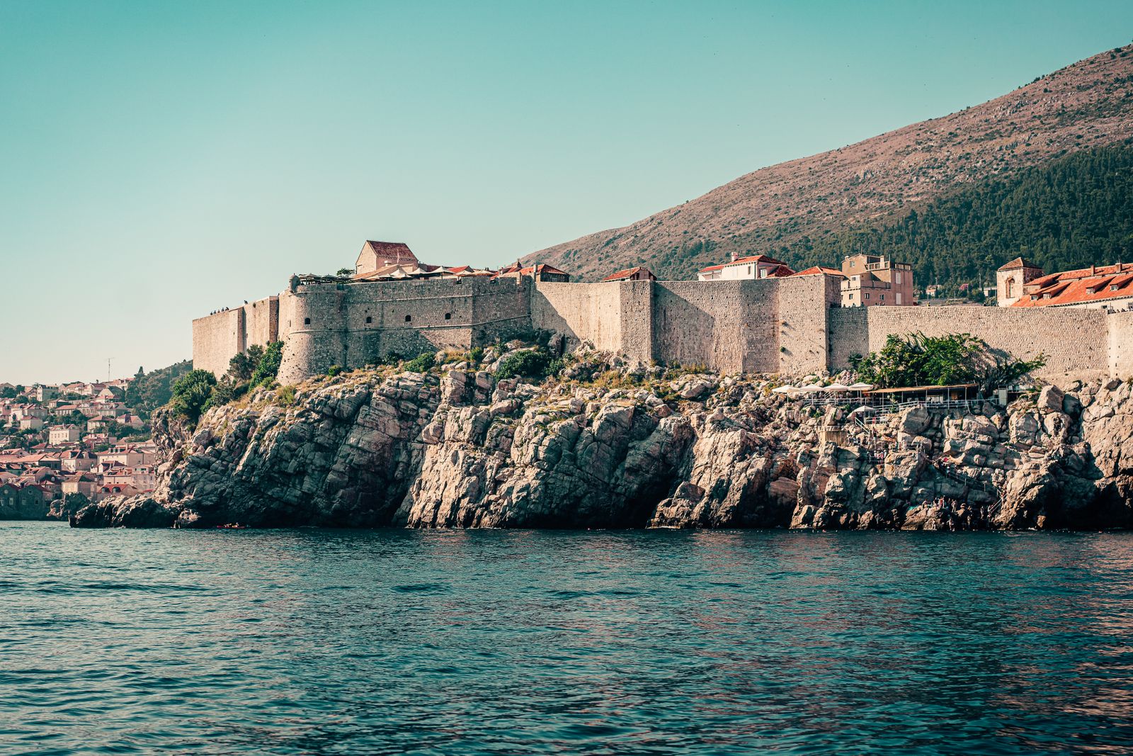 Dubrovnik's stone walls running along a rocky headland above the sea, seen from a boat