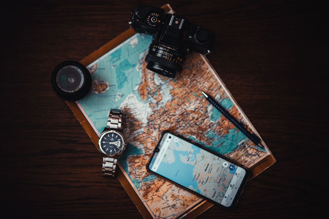 A flat lay of a Europe map with a phone, camera, watch and pen, the kit behind our esim reviews for European trips