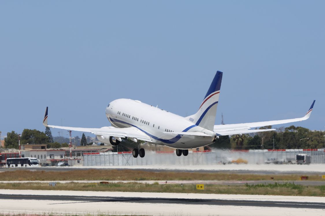 A white jet with blue and red tail stripes lifts off a runway on a clear day, as departures do from Gatwick Airport terminals