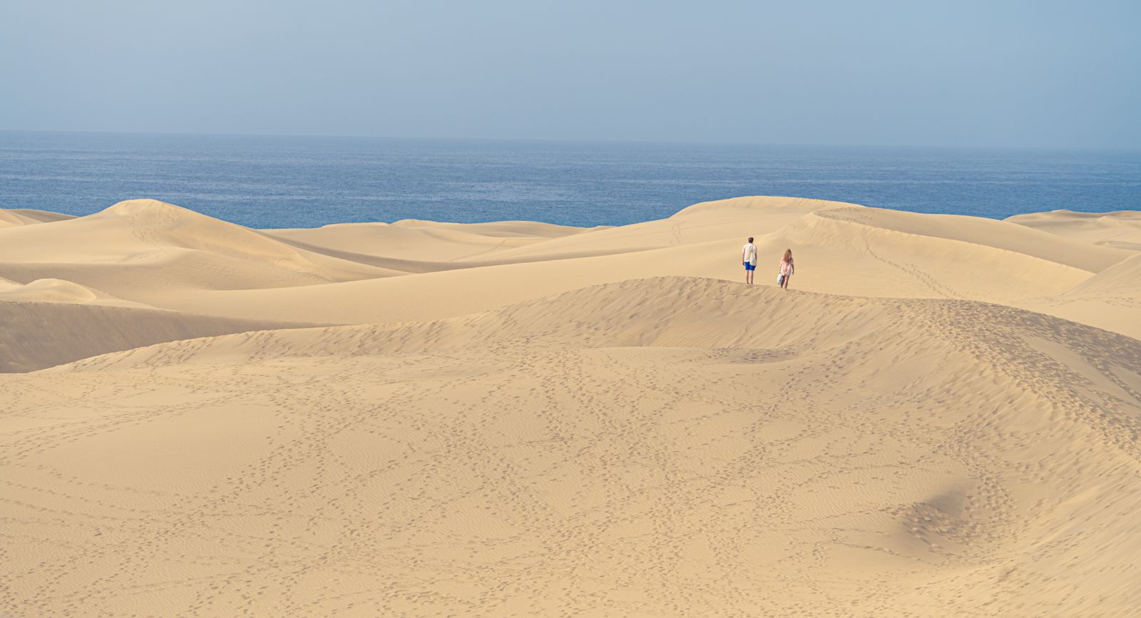 Two walkers on the golden Maspalomas dunes on Gran Canaria, with the Atlantic behind