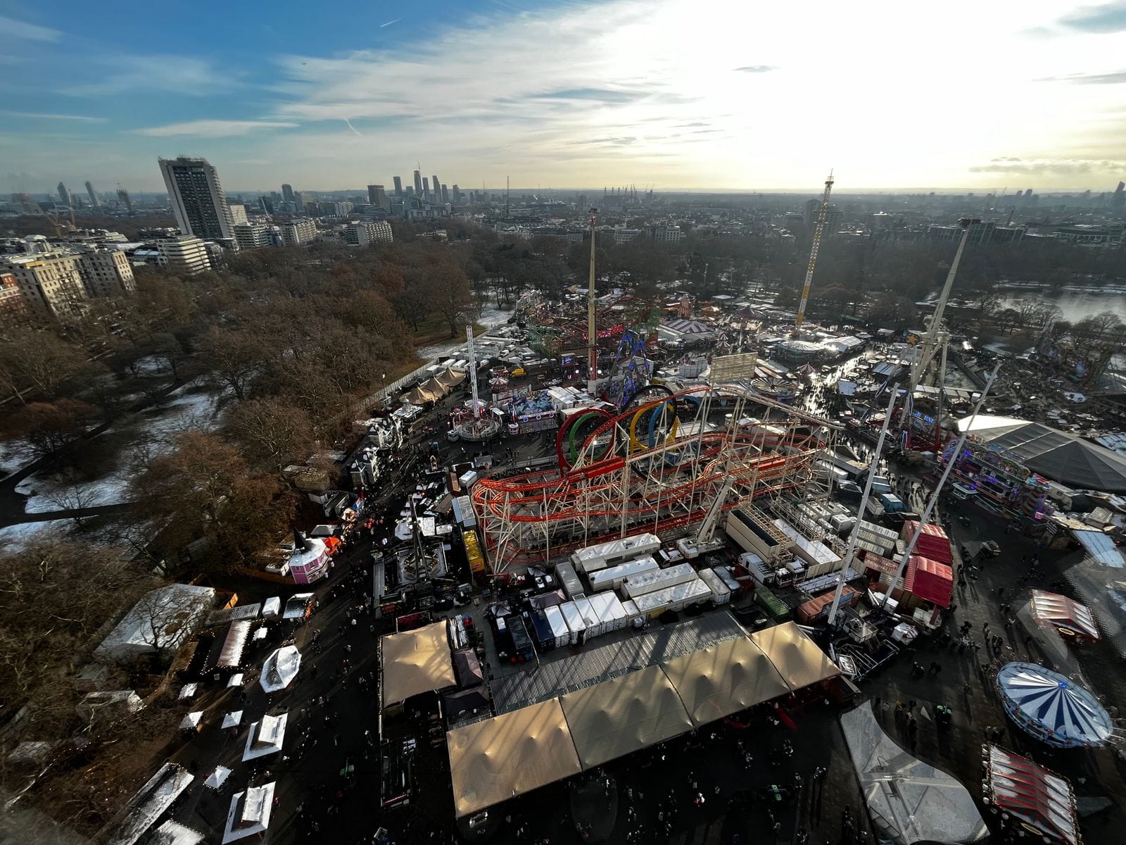 Aerial view of the Winter Wonderland funfair in Hyde Park, with rides and marquees among bare trees and the London skyline behind