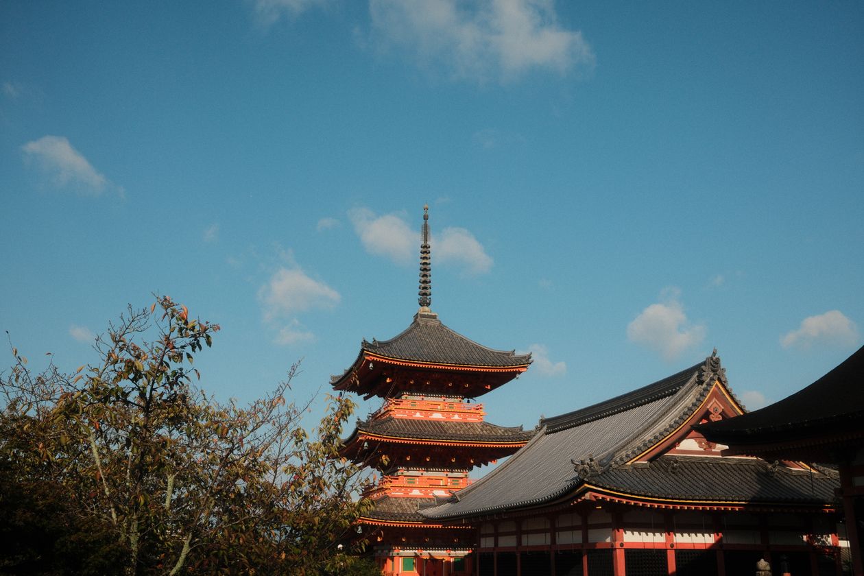 A red pagoda and temple roofs under a blue sky in Kyoto, Japan