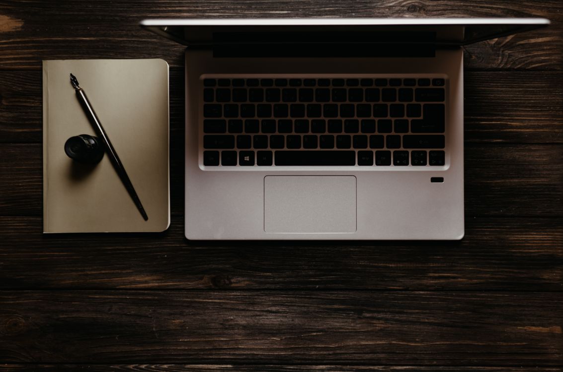 A laptop beside a notebook and pen on a dark desk, for writing up a Jet2 complaint and asking for a call back by email