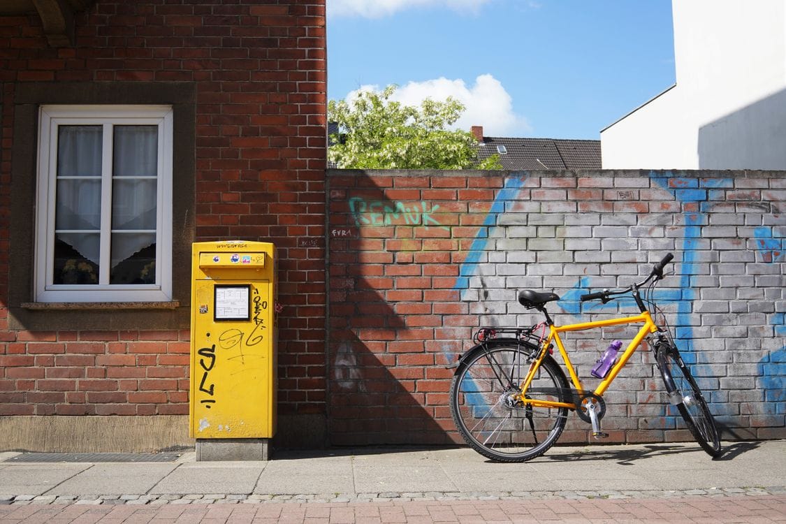 A yellow bicycle leaning against a brick wall beside a yellow postbox