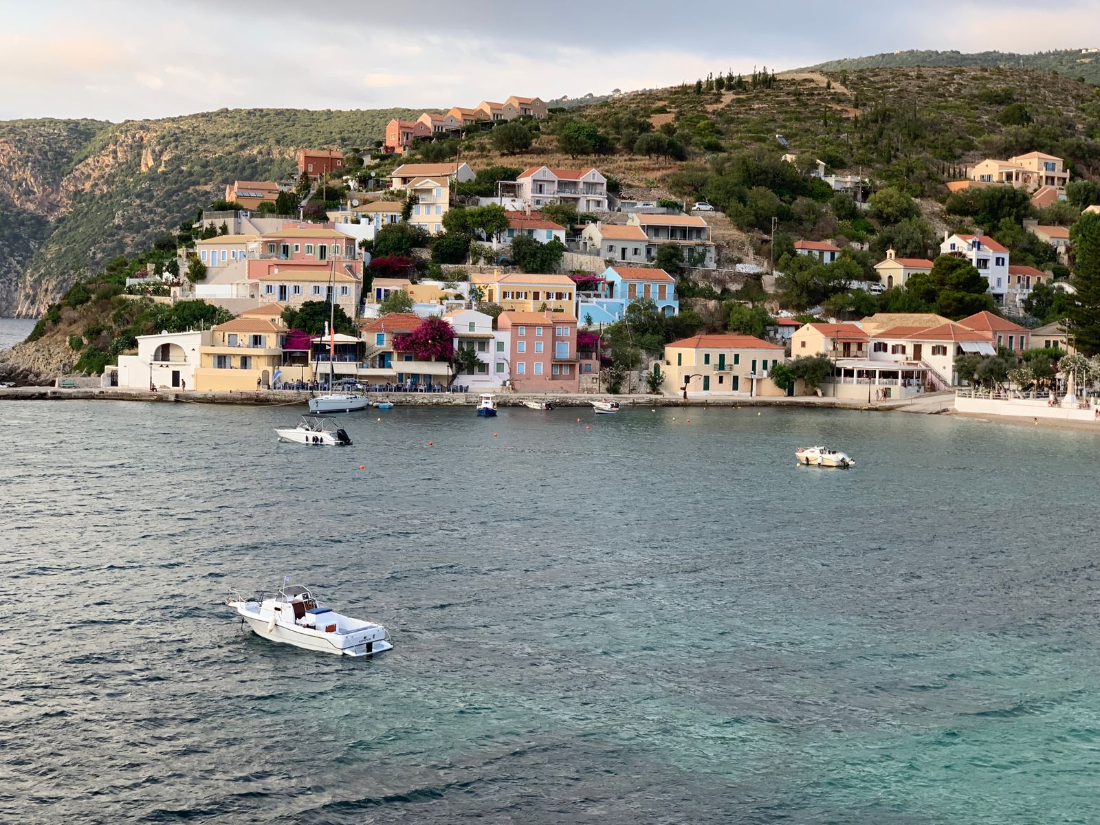 Pastel-coloured houses on the hillside above the bay at Assos village, Kefalonia, with small boats on the water