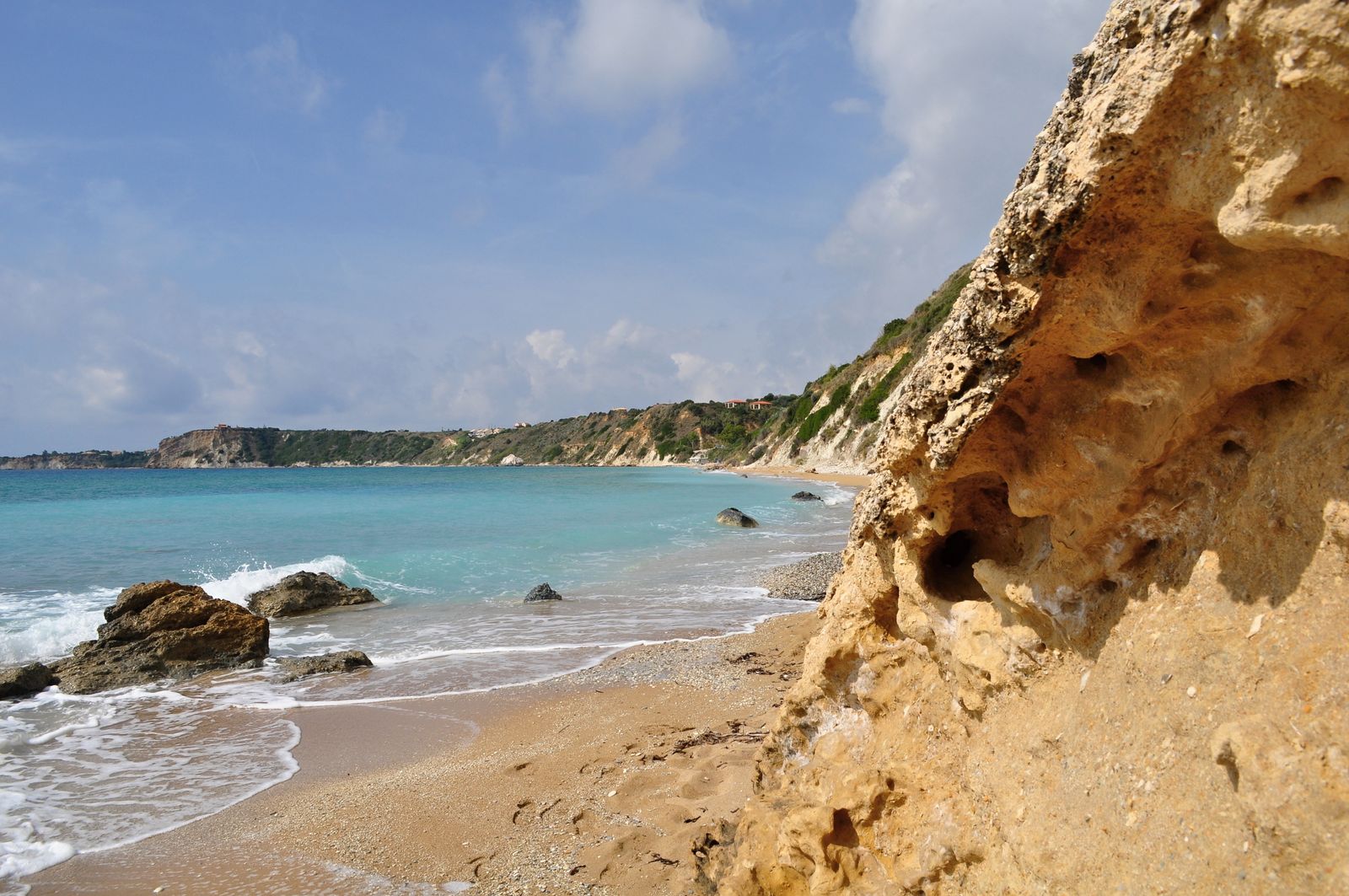 Sunlit rocky shore and pebble sand at Avithos Beach on Kefalonia with turquoise water