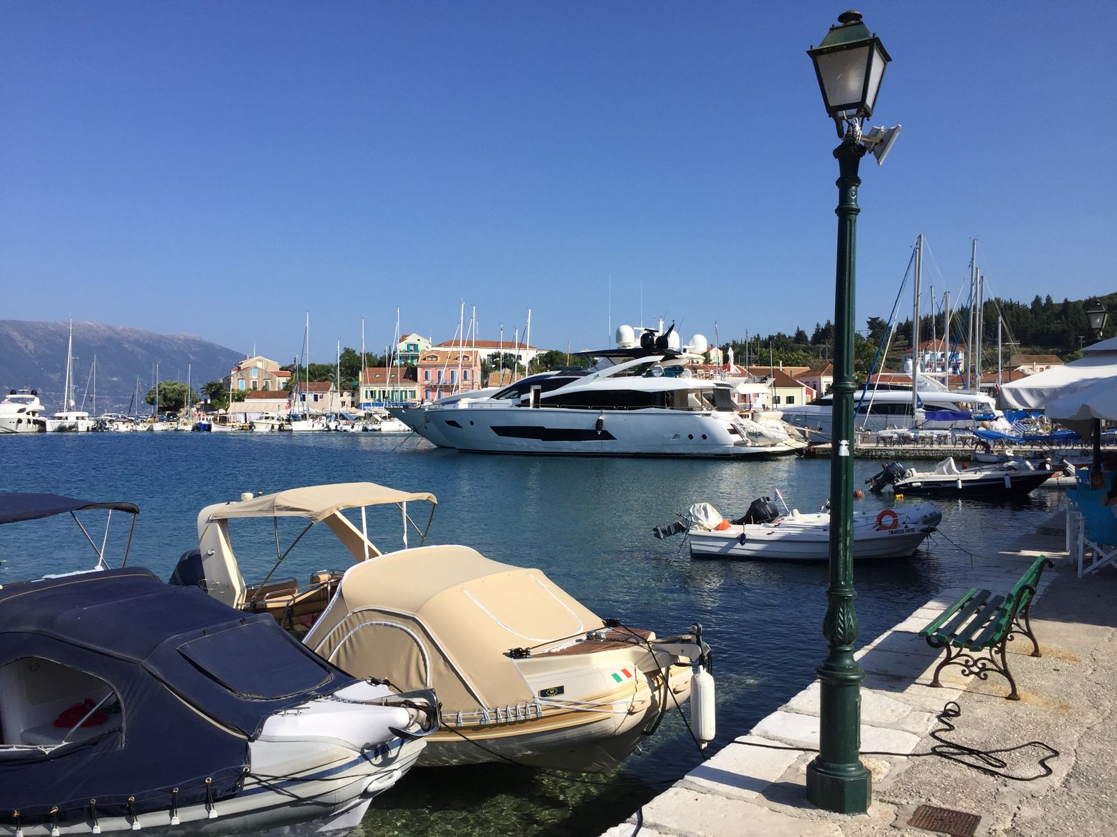Moored boats and yachts along the quay at Fiskardo harbour on Kefalonia with the village behind
