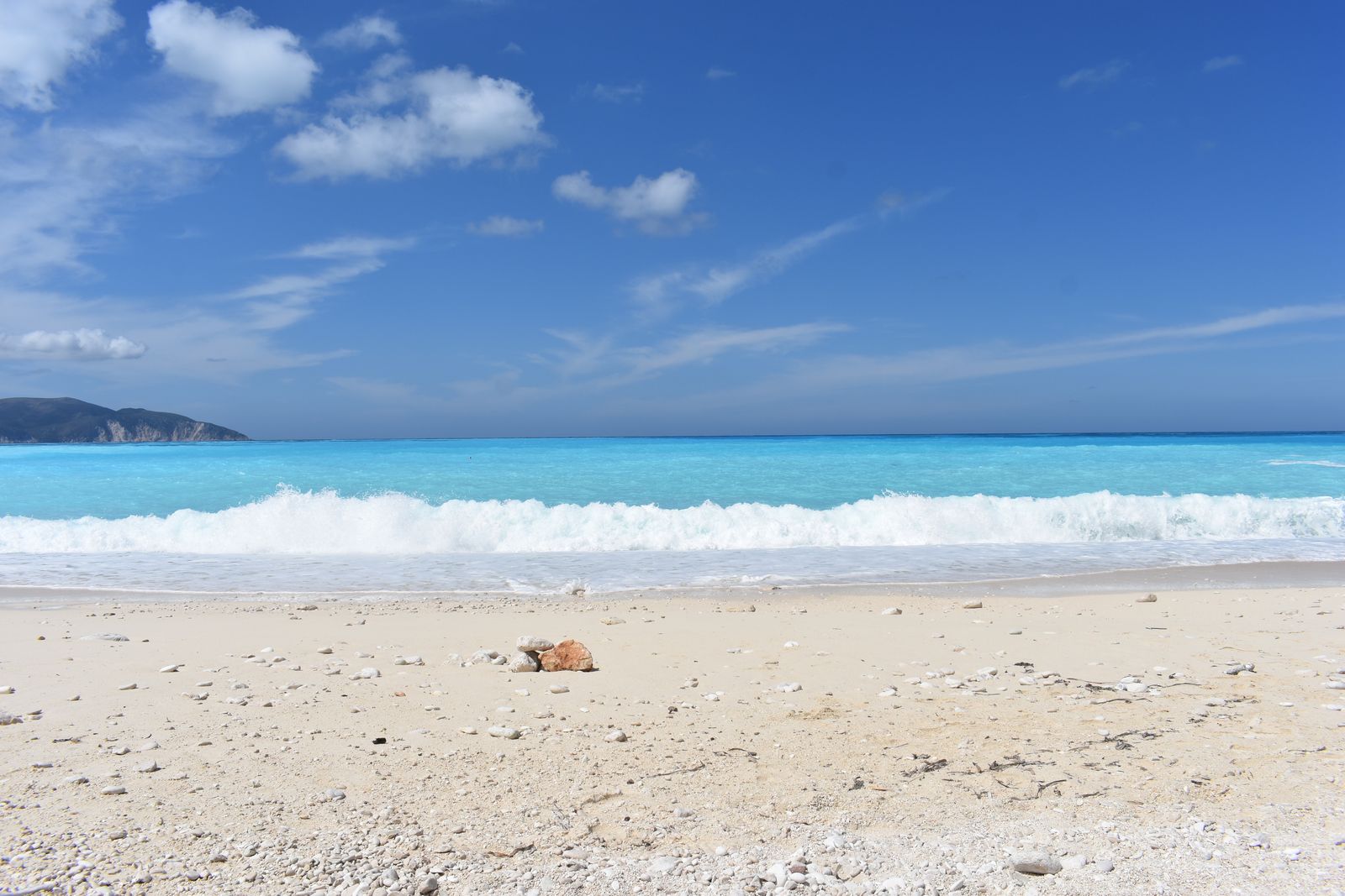 Waves breaking on a pale sand and pebble beach at Myrtos on Kefalonia under a blue sky