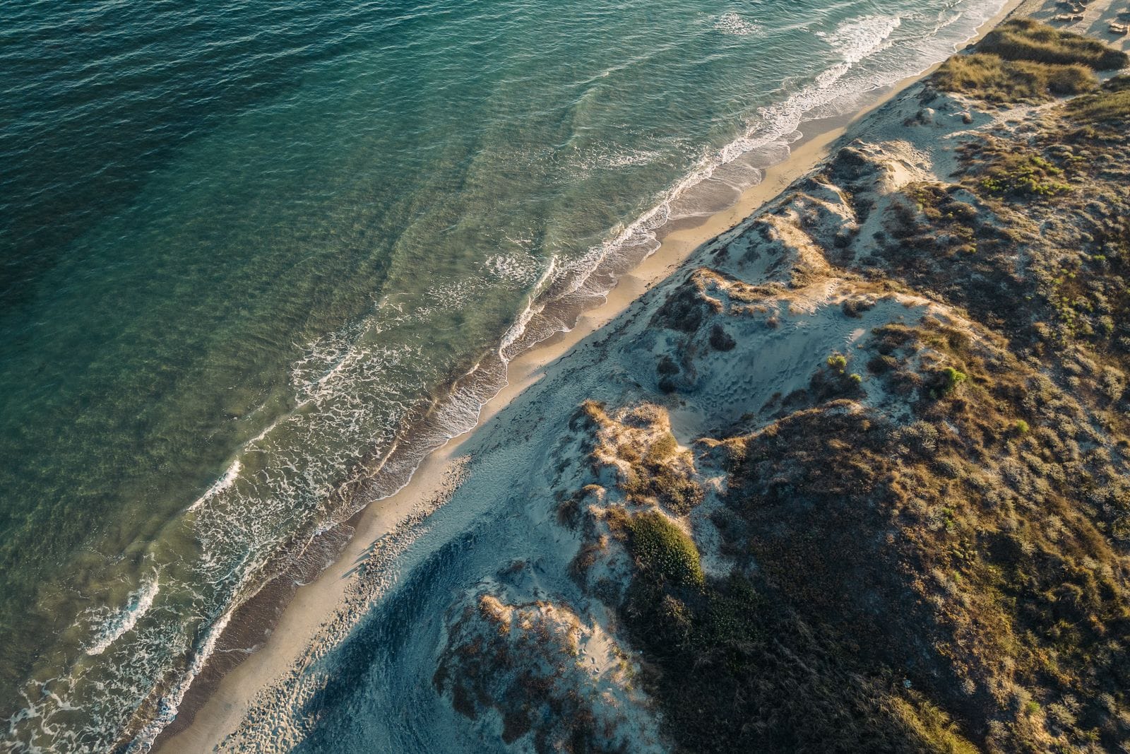 Aerial view of a long sandy Kos beach with turquoise water meeting dunes and scrub