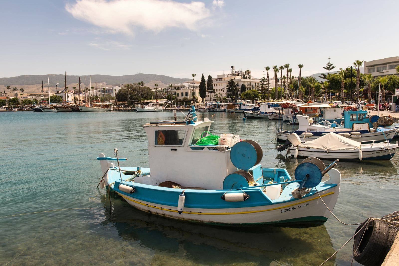 A blue and white wooden fishing boat moored in Kos harbour with the town and masts of moored yachts behind