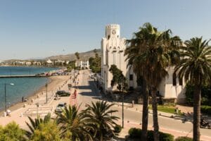 Is Kos expensive: the palm-lined waterfront promenade of Kos Town with the harbour and mountains of the Turkish coast beyond