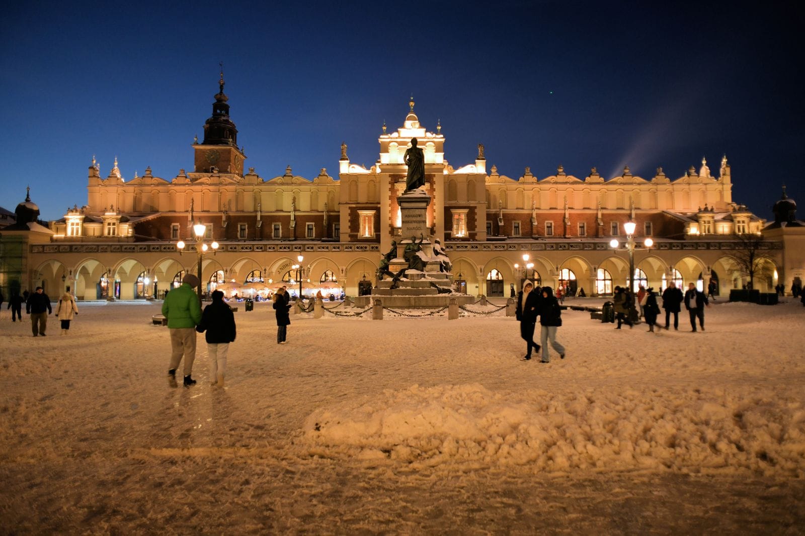 Kraków's Cloth Hall and the Mickiewicz Monument lit up at night across a snow-covered Main Market Square