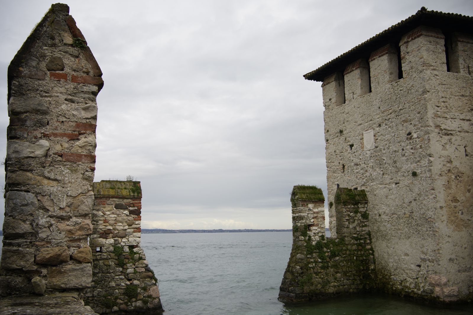Weathered stone walls of Scaliger Castle in Sirmione rising straight out of Lake Garda under a pale sky
