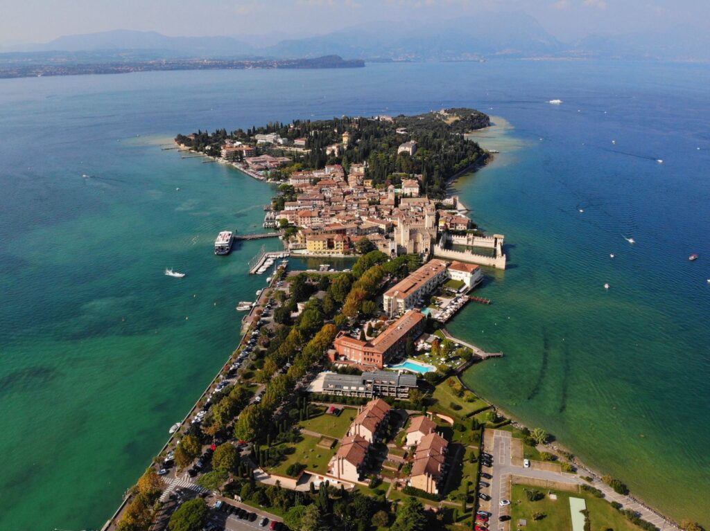 Is Lake Garda expensive: aerial view of the Sirmione peninsula reaching into turquoise Lake Garda, with mountains beyond