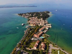 Is Lake Garda expensive: aerial view of the Sirmione peninsula reaching into turquoise Lake Garda, with mountains beyond