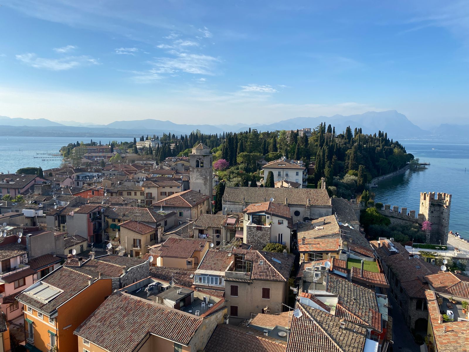 Terracotta rooftops of Sirmione old town with a castle tower and the lake behind, seen from above