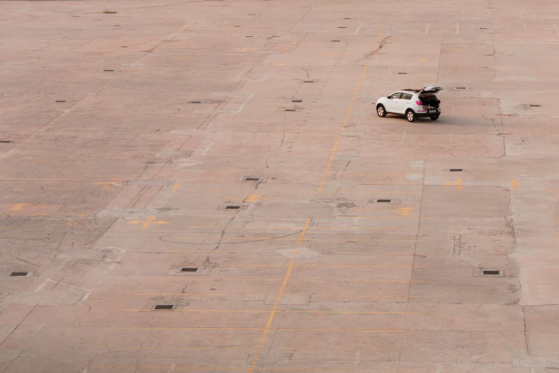 A white SUV with its boot open on a large empty car park, the kind of space where a Luton airport drop off ends and the bags come out