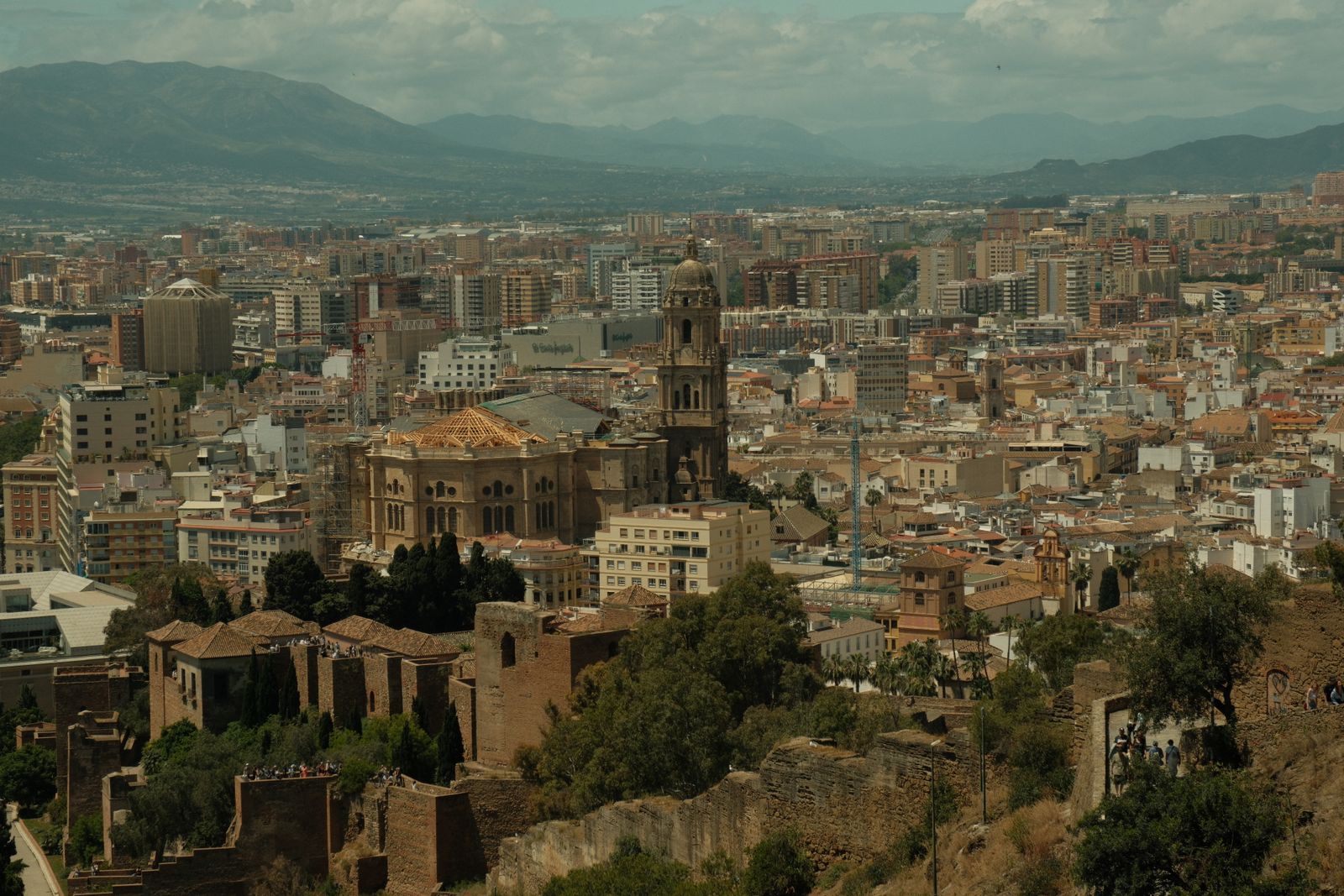 Old fortress walls on the hillside above Malaga, with the cathedral tower rising from the city and mountains behind