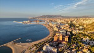 Is Malaga expensive: aerial view of Malaga's curved city beach, harbour and hills in warm evening light