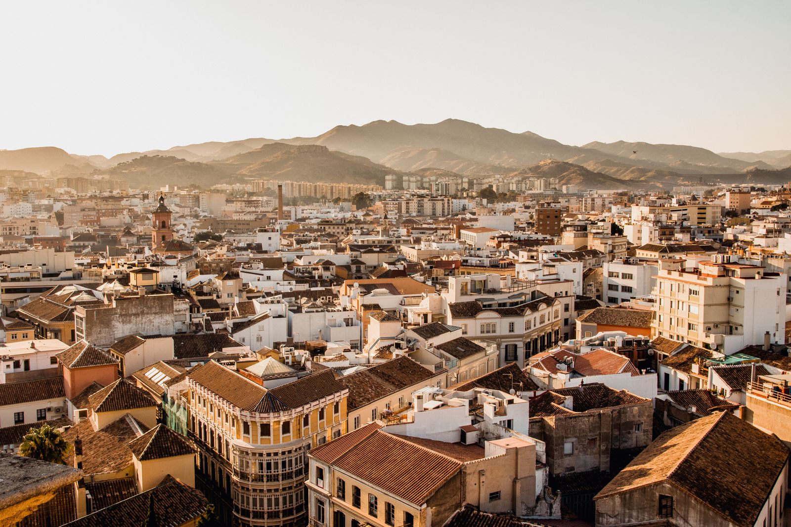Terracotta rooftops and narrow streets of Malaga's old centre in golden light, with hills behind