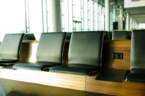 Rows of black airport seats beside a bright window with a power socket, a quiet corner for waiting at Manchester Airport Terminal 2