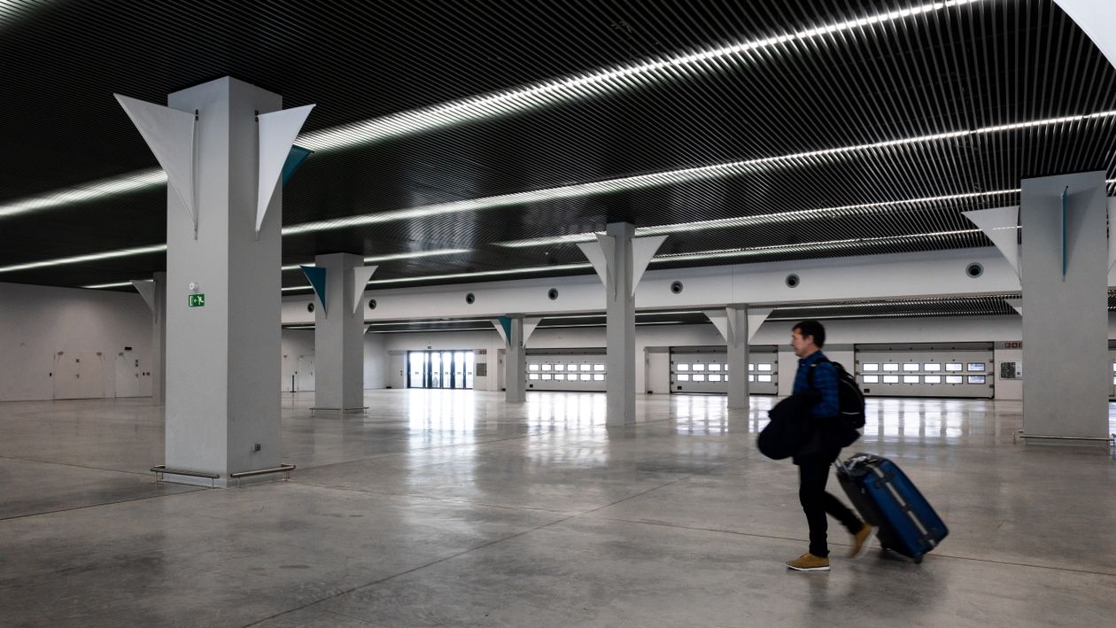 A traveller wheels a blue suitcase across a large, empty airport hall, as on the walk between Manchester Airport terminals