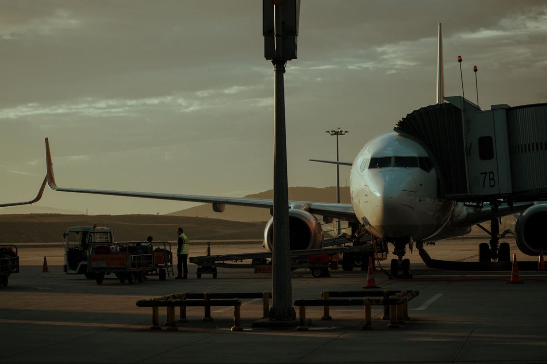 A passenger jet at an airport gate at dusk with baggage trolleys on the apron, as on a P&O Cruises charter flight