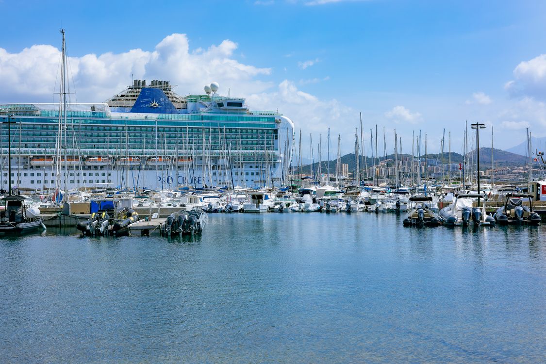A large cruise ship moored in a marina behind small boats, the ship a P&O Cruises fly-cruise flight check-in leads to