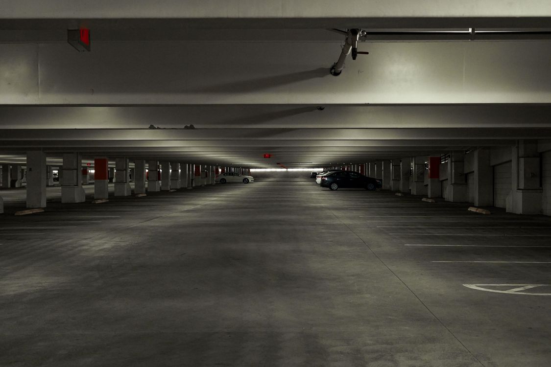 A quiet multi-storey car park with a few cars parked under strip lights, like the Short Stay car parks at the Stansted airport terminal