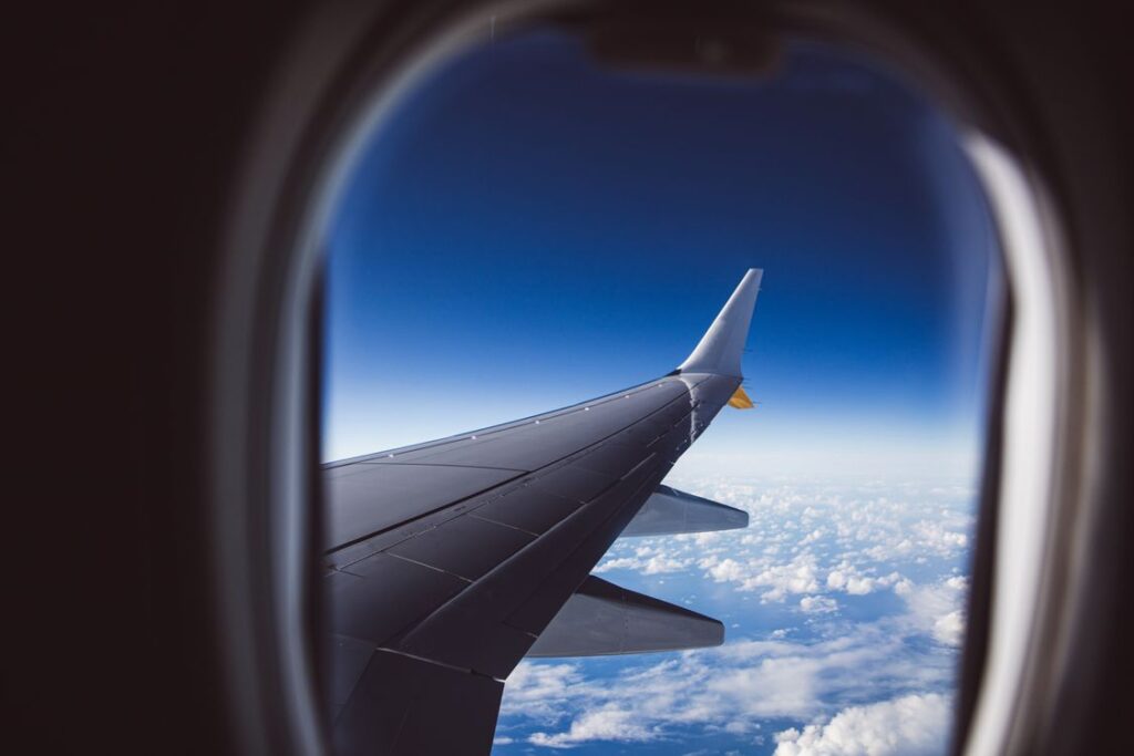A grey wing and winglet over white cloud seen through an aircraft window, the view after leaving the Stansted airport terminal