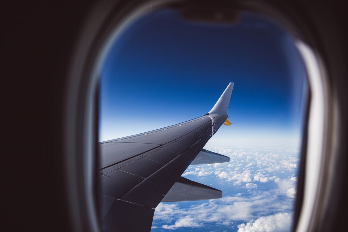 A grey wing and winglet over white cloud seen through an aircraft window, the view after leaving the Stansted airport terminal
