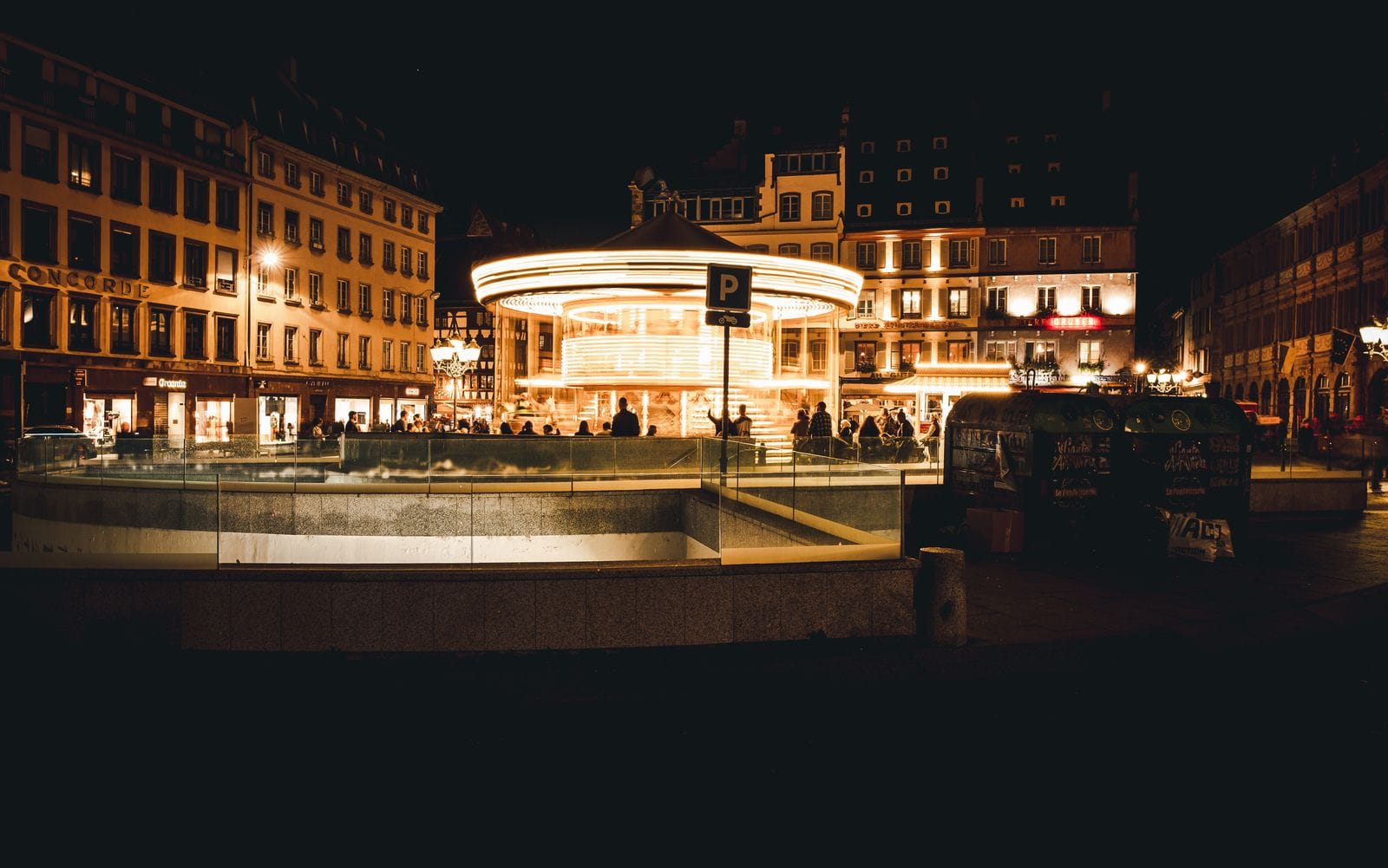A lit-up carousel turning in a square in central Strasbourg at night, with old townhouses behind
