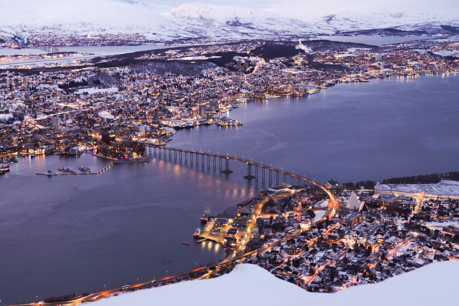 Aerial view of Tromso at twilight with the bridge across the fjord and snowy mountains beyond
