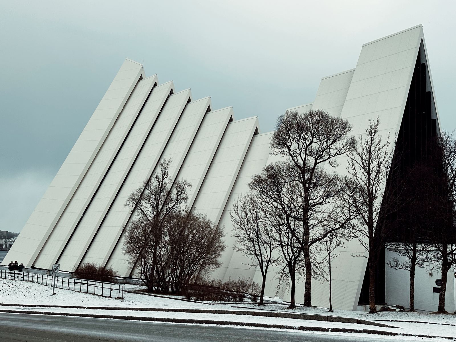 The white angled Arctic Cathedral in Tromso with bare trees and light snow on the ground