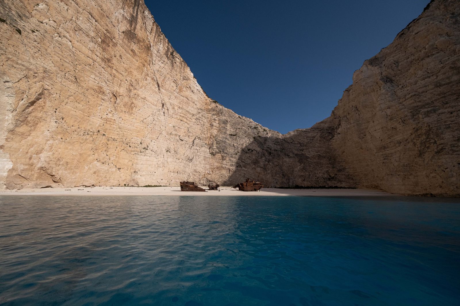 A rusting shipwreck on the sand of Navagio Beach, Zakynthos, below tall pale cliffs, seen from the sea